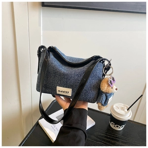 Detail of denim bucket bag with teddy bear charm and mdd137 label in urban setting