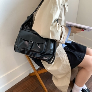 Große schwarze Schultertasche aus glänzendem Leder mit Schnalle getragen zum Trenchcoat