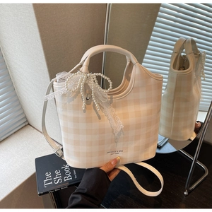 Close-up of beige checkered tote bag with pearl lace bow charm and crossbody strap