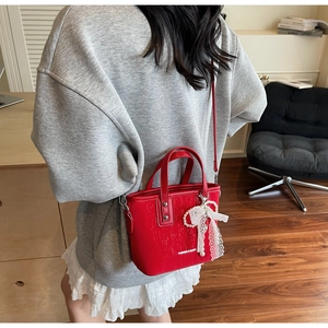 Detail of red crossbody bag featuring vertical texture, lace bow, and pearl charm