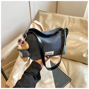 Detail of denim bucket bag with black patent leather strap and cute bear charm accessory