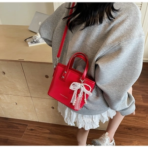 Red fashion tote bag with lace bow and pearl charm shown on model in a minimalist setting
