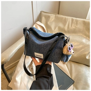 Detail of denim shoulder bag featuring a cute bear pendant and leather strap