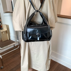 Detail der schwarzen glänzenden Ledertasche mit Metallschnalle auf beige Trenchcoat