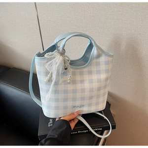 Detailed view of checkered tote bag with pearl bow charm and brand logo on book