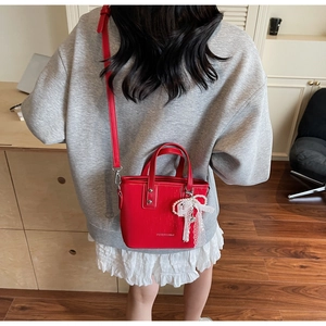 Detail of red bucket bag with lace pearl bow charm and long shoulder strap on model