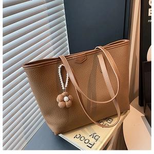 Détail du cabas en cuir caramel avec charm perle et fleur en peluche posé sur des livres