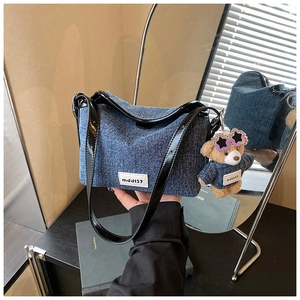 Close-up of denim shoulder bag with brand label and cute matching bear plush pendant