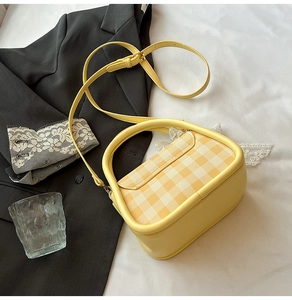 Detail of yellow checkered handbag with top handle and matching shoulder strap on white fabric