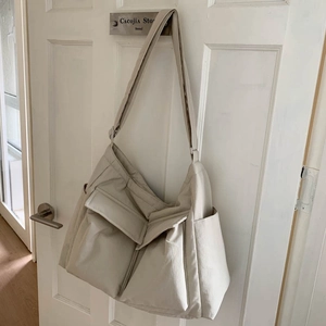Detail view of large beige canvas crossbody bag hanging on a door with multiple pockets