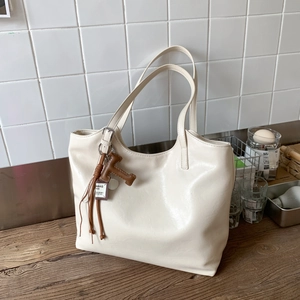 Detalle de un bolso tote de cuero PU crema con un colgante de borla marrón