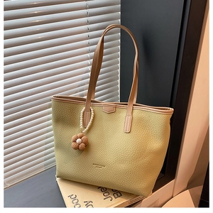 Détail d'un sac cabas jaune avec breloque fleurie et texture de cuir sur des livres