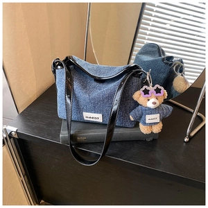 Detail of denim bucket bag with leather strap, logo label and cute teddy bear charm
