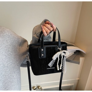 Detail of black PU leather bucket bag with elegant pearl and lace bow charm decoration