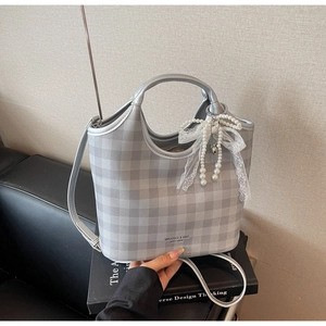 Detail of grey plaid tote bag featuring a lace bow and pearl charm on a leather seat