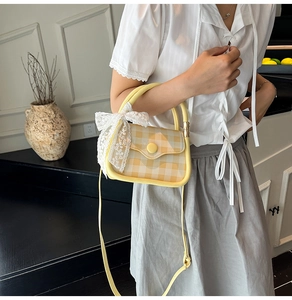 Detail of light yellow plaid handbag featuring a white lace bow and round button clasp