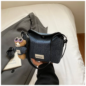 Detailed shot of denim bucket bag with black trim and cute teddy bear charm