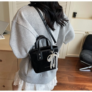 Detail of black leather crossbody bag with pearl lace bow and adjustable shoulder strap