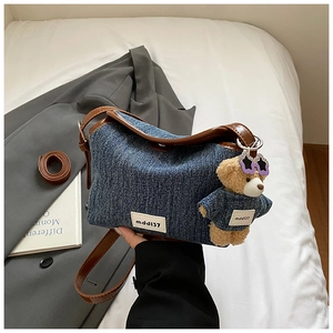 Detail of denim bucket bag featuring a brown leather strap and a cute bear charm