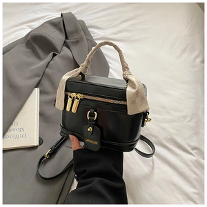 Détail d'un sac boîte en cuir noir avec poignée enrubannée et finitions dorées