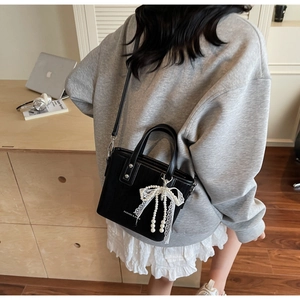 Detail of a black vertical striped tote bag with pearl lace bow and leather strap