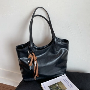 Detail of a black leather tote bag with a brown horse charm on a modern gray cushion