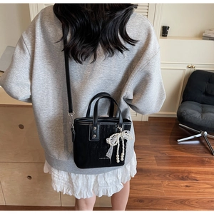 Detail of black textured bucket bag featuring a pearl lace bow and side-carry strap
