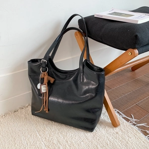 Vista de detalle del bolso tote de cuero sintético negro brillante con borla marrón