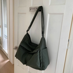 Detail of a large army green canvas messenger bag featuring utility pockets on a white door