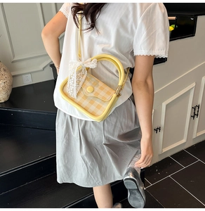 Detail of yellow plaid handbag featuring a decorative white lace bow and round buckle