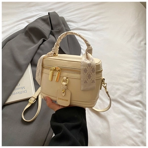 Détail d'un mini sac boîte crème avec poignée en foulard décoratif et étiquette métallique