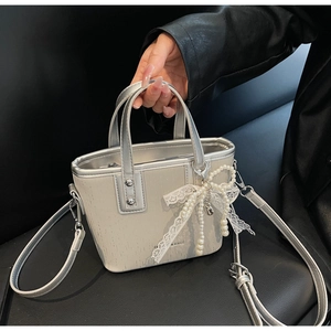 Detail of cream crossbody bag with silver handles and elegant lace pearl bow charm
