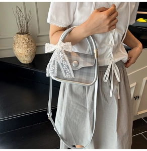 Detail of grey plaid handbag featuring a white lace bow and silver metal handle