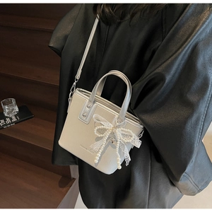 Close-up of light gray crossbody bag with lace bow, pearl charm and fashion design text