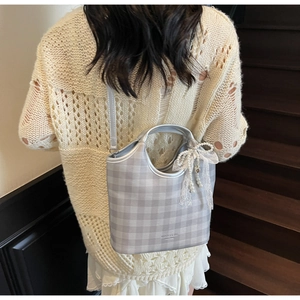 Close-up of checkered tote bag with silver handle, lace bow charm, and pearl details