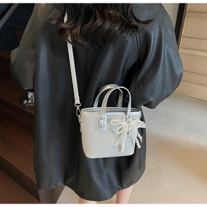 Detail of silver bucket bag with pearl lace bow charm on wood staircase
