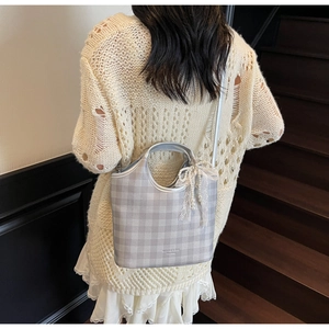 Detail of silver plaid tote bag with lace pearl bow charm on model in soft lighting