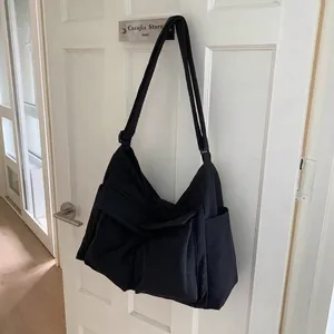Detail of black canvas messenger bag featuring a large front flap pocket and wide strap
