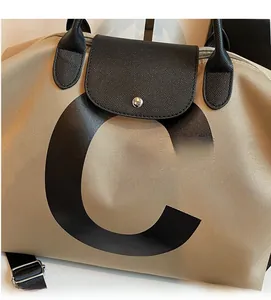 Close-up of khaki travel tote with black leather trim and bold letter C design