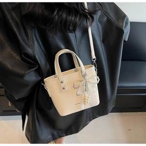 Detail of cream white faux leather bucket bag with pearl lace pendant and fashion logo