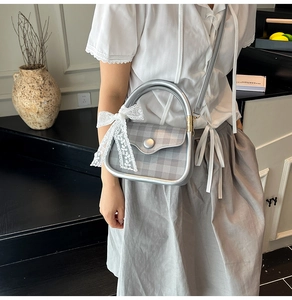 Detail of grey plaid handbag with white lace bow decoration and silver metal frame