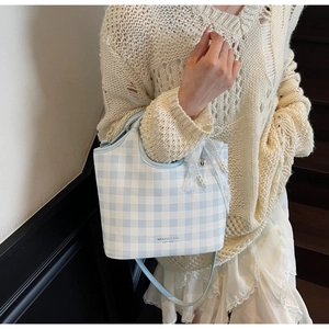 Detail of blue gingham tote bag featuring a pearl charm and lace bow on a classic pattern