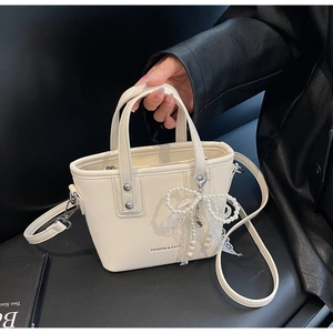 Detail of a creamy white mini tote bag with a pearl lace bow charm and thin strap