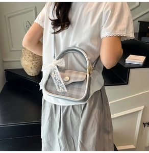 Detail of silver checkered crossbody bag with metal handle and white lace bow decoration