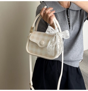 Detail of checkered crossbody bag with large white lace bow and round metal buckle