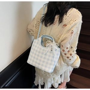 Close-up of light blue gingham shoulder bag with pearl lace bow charm and brand logo