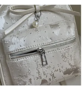Detailed macro view of white jacquard fabric with silver sequins and a pearl bow charm