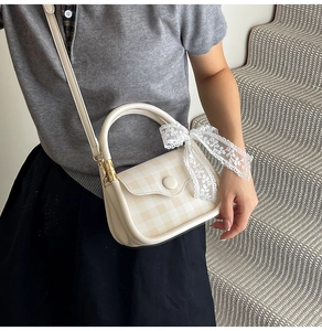 Detail view of cream-white crossbody bag featuring a lace bow and plaid pattern flap