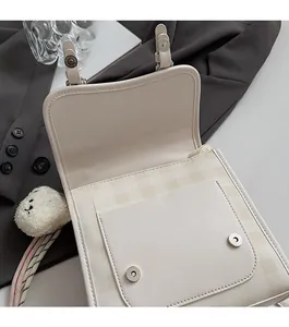 Detail of cream shoulder bag featuring magnetic buckle closure and checkered lining detail