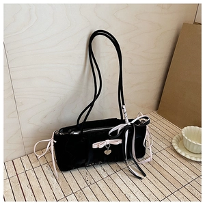 Detailed close-up of a black patent leather shoulder bag featuring a pink bow and heart charm